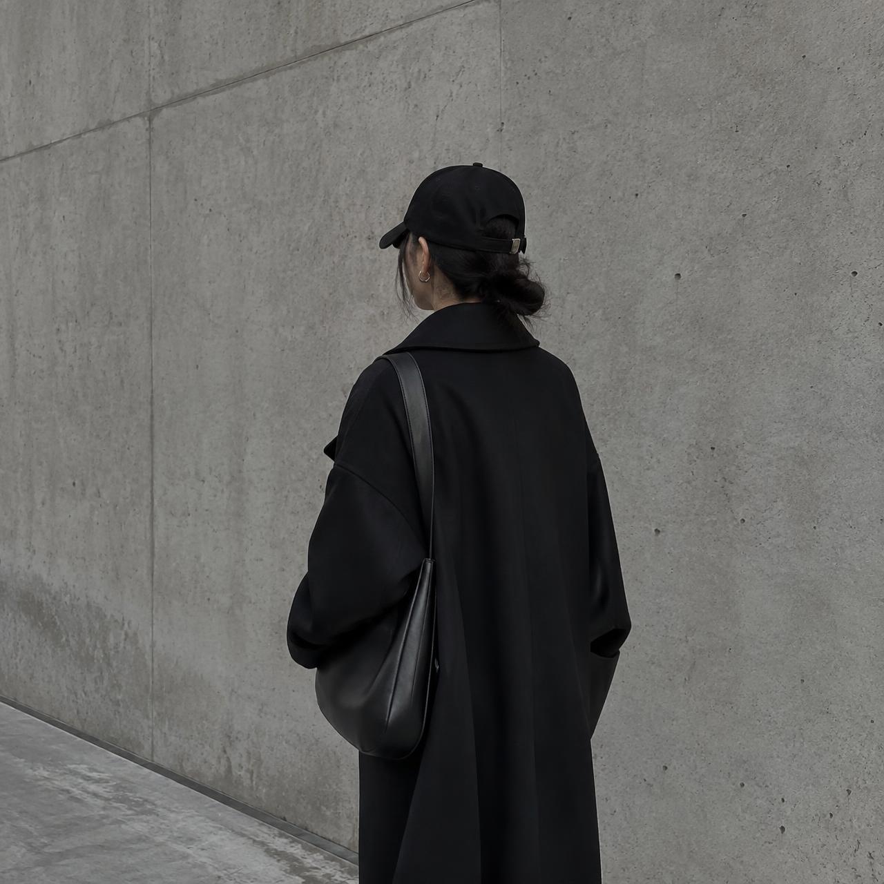 Creator in a black coat beside a concrete wall