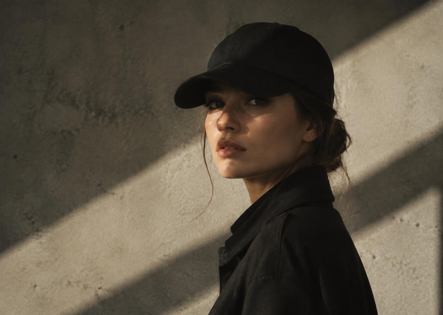 Editorial portrait in a black cap against a concrete wall